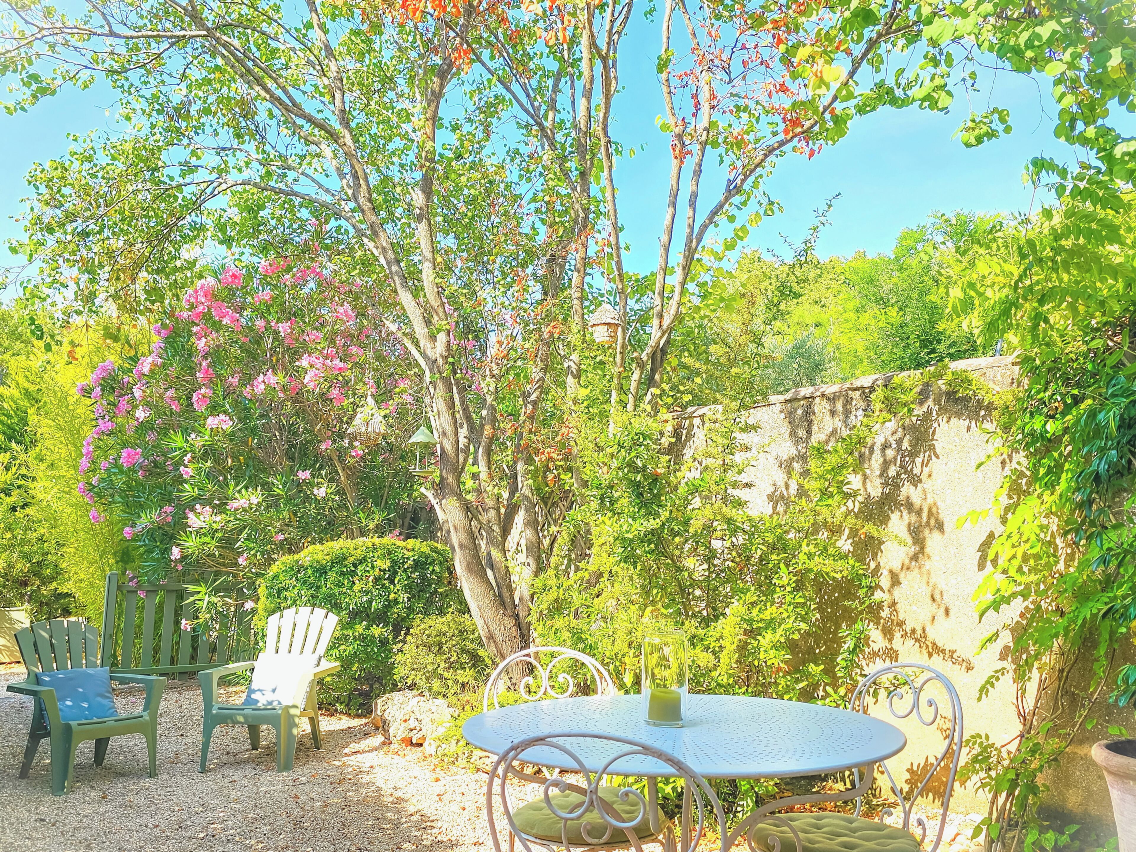 Une terrasse de jardin avec une table ronde, deux chaises et une mangeoire à oiseaux.