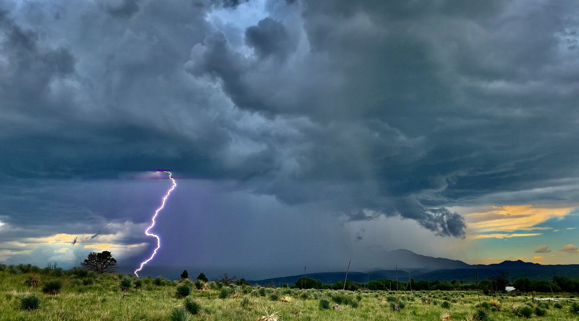 A landscape with a lightning strike and mountains in the background.