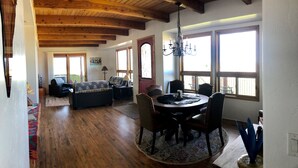 Un espacio habitable amplio con techo de madera, una mesa de comedor con sillas y ventanas grandes que dejan entrar luz natural.