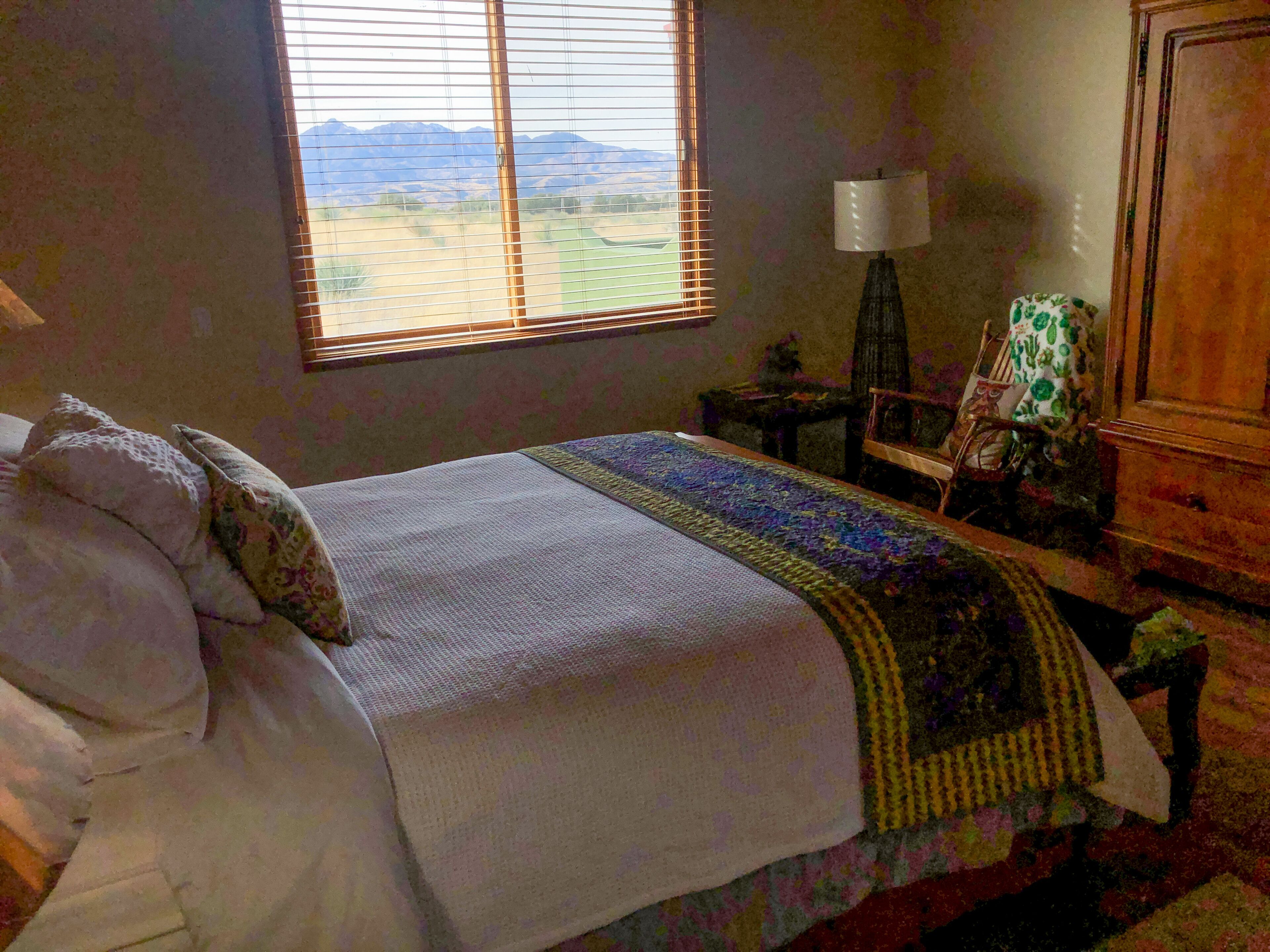 A bedroom with a bed, a window with a view, a lamp, and a chair.