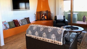 Una sala de estar acogedora con chimenea, un sofá con cojines estampados, un sillón de cuero y un televisor montado en la pared.
