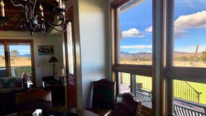 Comedor con vistas a un campo verde y montañas a través de amplios ventanales.