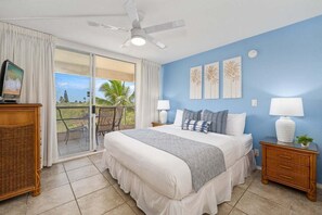 A bedroom with a bed, two bedside tables, a ceiling fan, and a view of the outdoors.