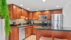A modern kitchen with wooden cabinets, stainless steel appliances, and a granite countertop. - Remodeled 2BD Condo Across Beach Pool AC - Maui Banyan P301 (Kihei)