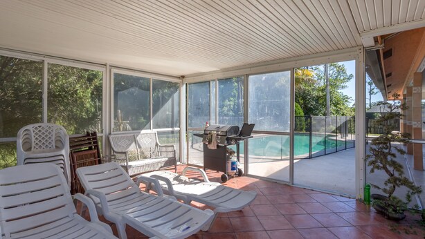 A covered outdoor area with white plastic chairs, a grill, and a view of a swimming pool. - Spacious property in a quiet neighborhood, 30% discount for stays over 28 days (Lake Worth)