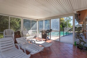 A covered outdoor area with white plastic chairs, a grill, and a view of a swimming pool. - Spacious property in a quiet neighborhood, 30% discount for stays over 28 days (Lake Worth)