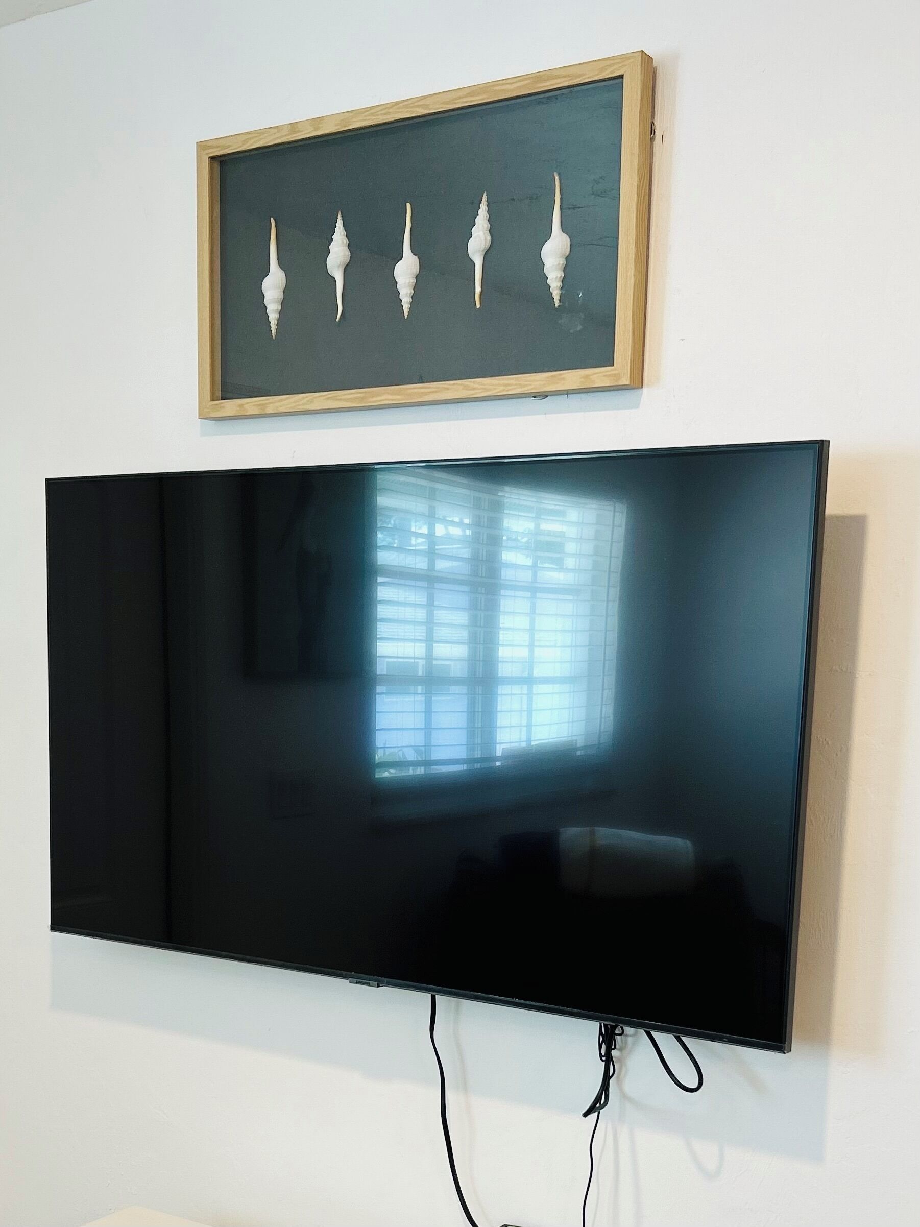 A flat-screen TV mounted on a wall with a framed picture above it.