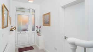 Un couloir avec une porte blanche, une petite table sur laquelle est posée une plante en pot et un tableau encadré au mur.