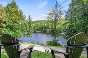 Two Adirondack chairs facing a lake surrounded by trees.