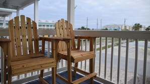 Two wooden Adirondack chairs on a wooden deck with a view of a distant building and a cloudy sky. - Steps to the gorgeous Mexico Beach! (Mexico Beach)