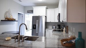 A modern kitchen with white cabinets, a stainless steel refrigerator, a built-in dishwasher, and a marble countertop. - Steps to the gorgeous Mexico Beach! (Mexico Beach)