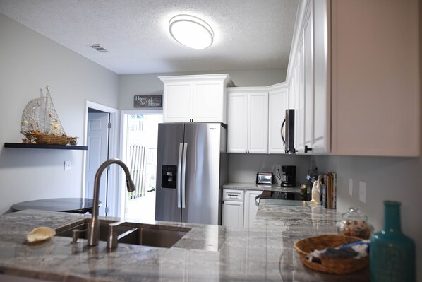 A modern kitchen with white cabinets, a stainless steel refrigerator, a built-in dishwasher, and a marble countertop.
