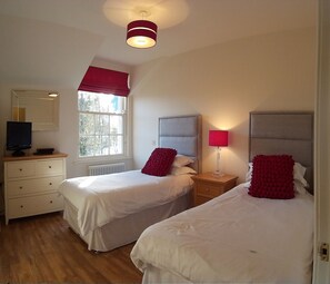 A bedroom with two beds, a dresser, a TV, and a window with a view of trees. - The Gate Lodge (Ballyclare)