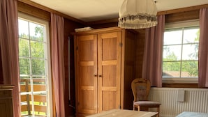 Ein Zimmer mit Holzboden, einem großen Kleiderschrank, einer Bank, einem Tisch und einem Bett.