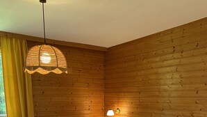 Ein Zimmer mit Holzwänden, einem Doppelbett, einem Sessel, einem Nachttisch und einer Hängelampe.