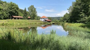 Eine friedliche Seelage mit einem Haus mit rotem Dach und weißen Wänden, umgeben von üppigem Grün und Bäumen.