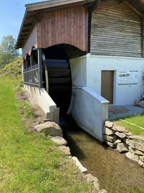 A building with a wooden exterior and a concrete entrance leading to a water channel. - Ferienidylle Brunnersäge (Achslach)