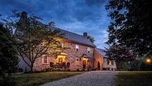 A stone building with a gravel driveway and a well-lit entrance. - The Stone House Between the Streams (Gap)