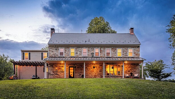 A two-story stone house with a covered porch and a garage. - The Stone House Between the Streams (Gap)