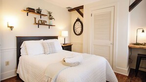 A neatly arranged bedroom with a bed, bedside tables, a wall clock, and a shelf with decorative items. - The Stone House Between the Streams (Gap)