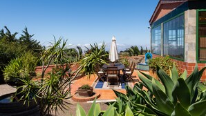 Un espace patio aménagé avec une table et des chaises, entouré de plantes en pot et agrémenté d’une fontaine décorative.
