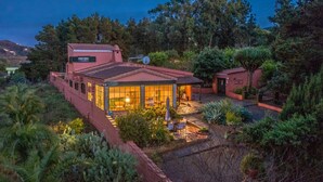 Une maison à deux étages dotée d’un patio, entourée d’une végétation luxuriante et d’arbres.