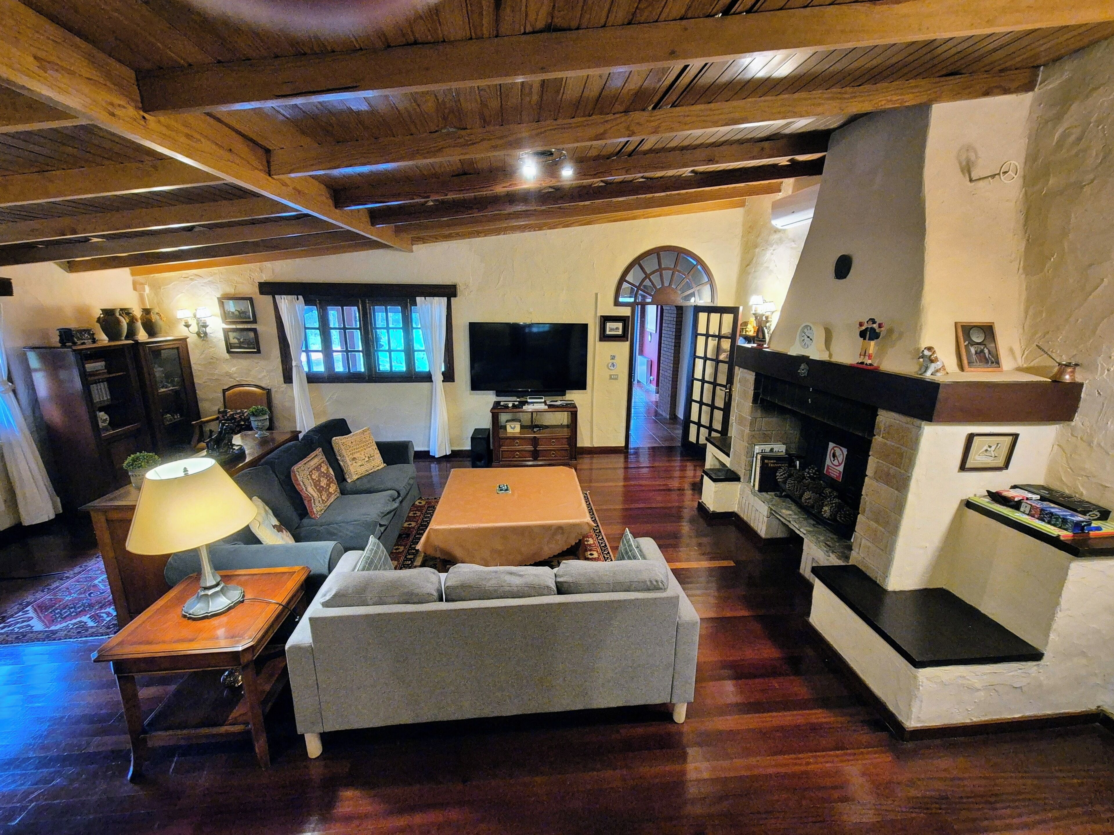 Una sala de estar con sofá, mesa de centro, televisor, chimenea y vigas de madera en el techo.