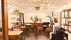 A cozy cafe interior with wooden tables and chairs, string lights, and potted plants. - Pop Up Hotel Krone Zürich (Zürich)