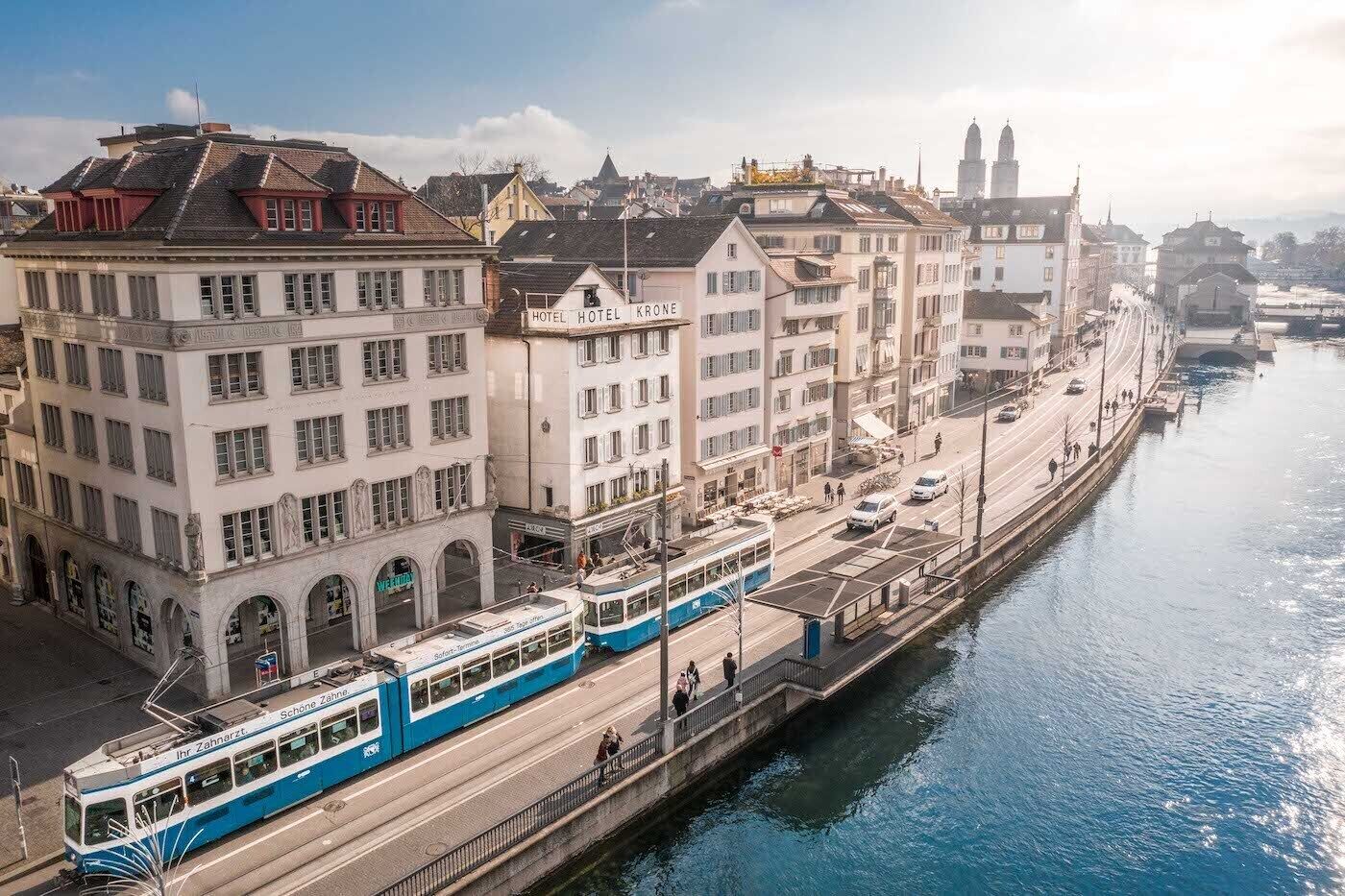 A tram line running alongside a canal with buildings on either side, including a hotel named 'HOTEL KRONE'.