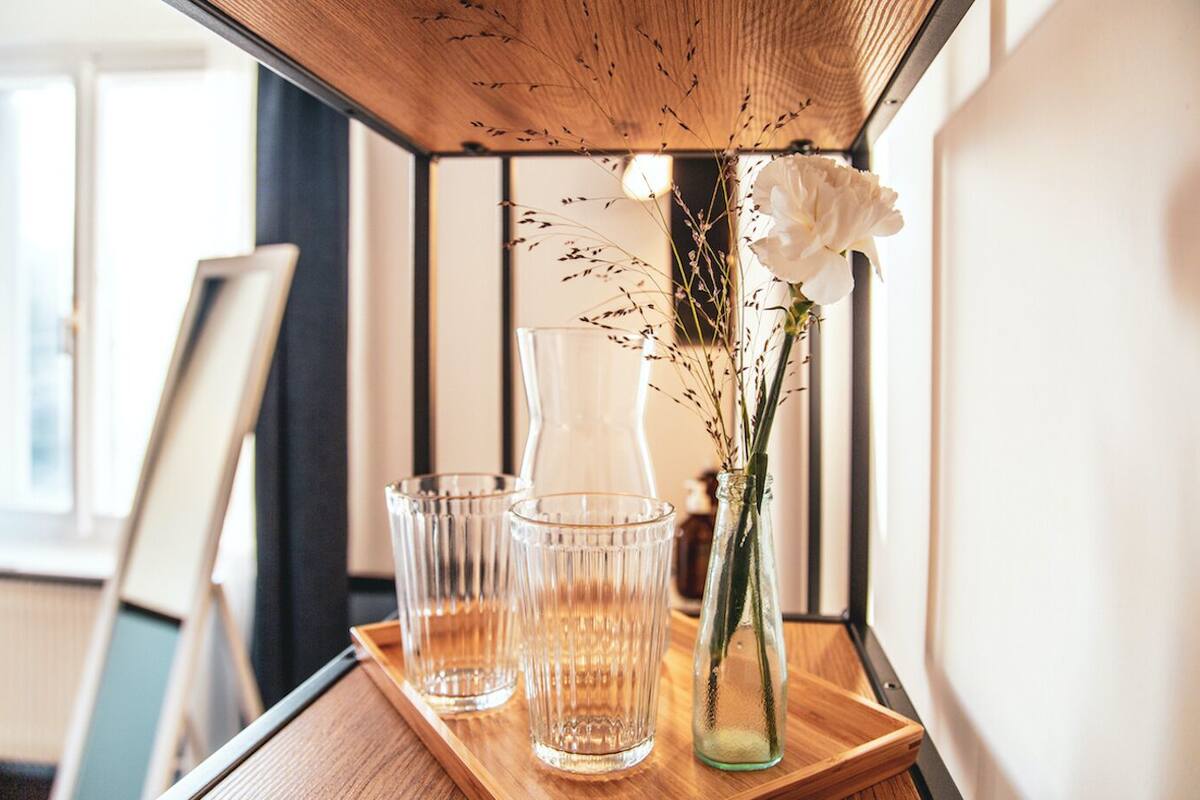 A wooden tray with three clear glasses and a vase with a white flower and dried plants.