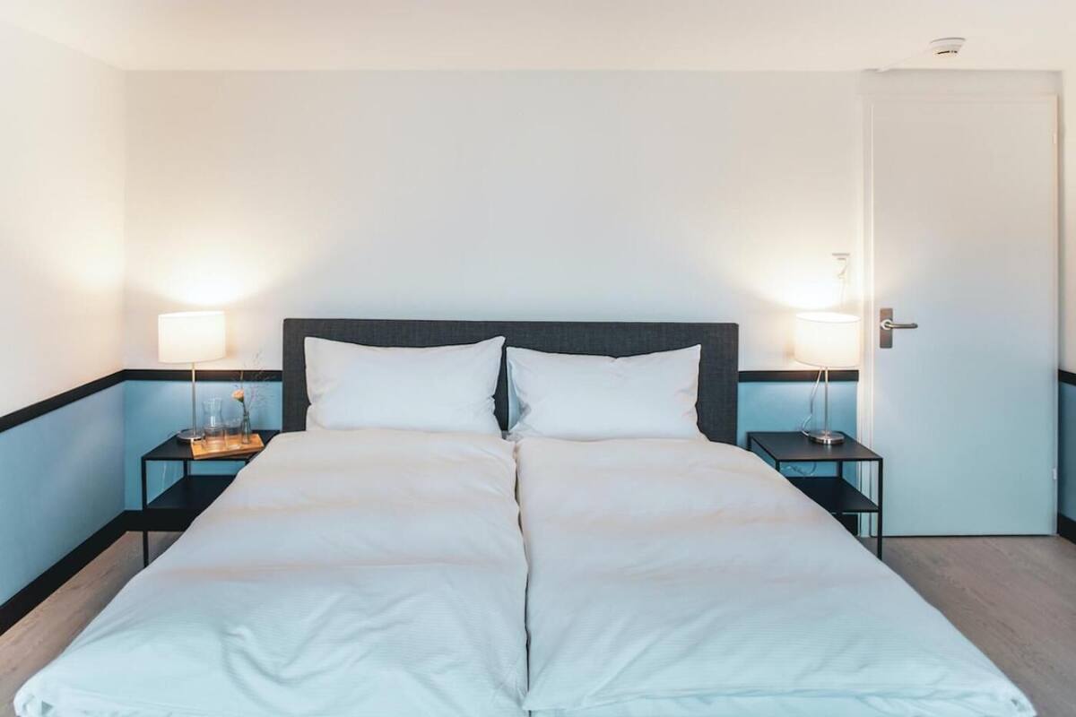 A double bed with white bedding, two bedside tables with lamps, and a door to the right.