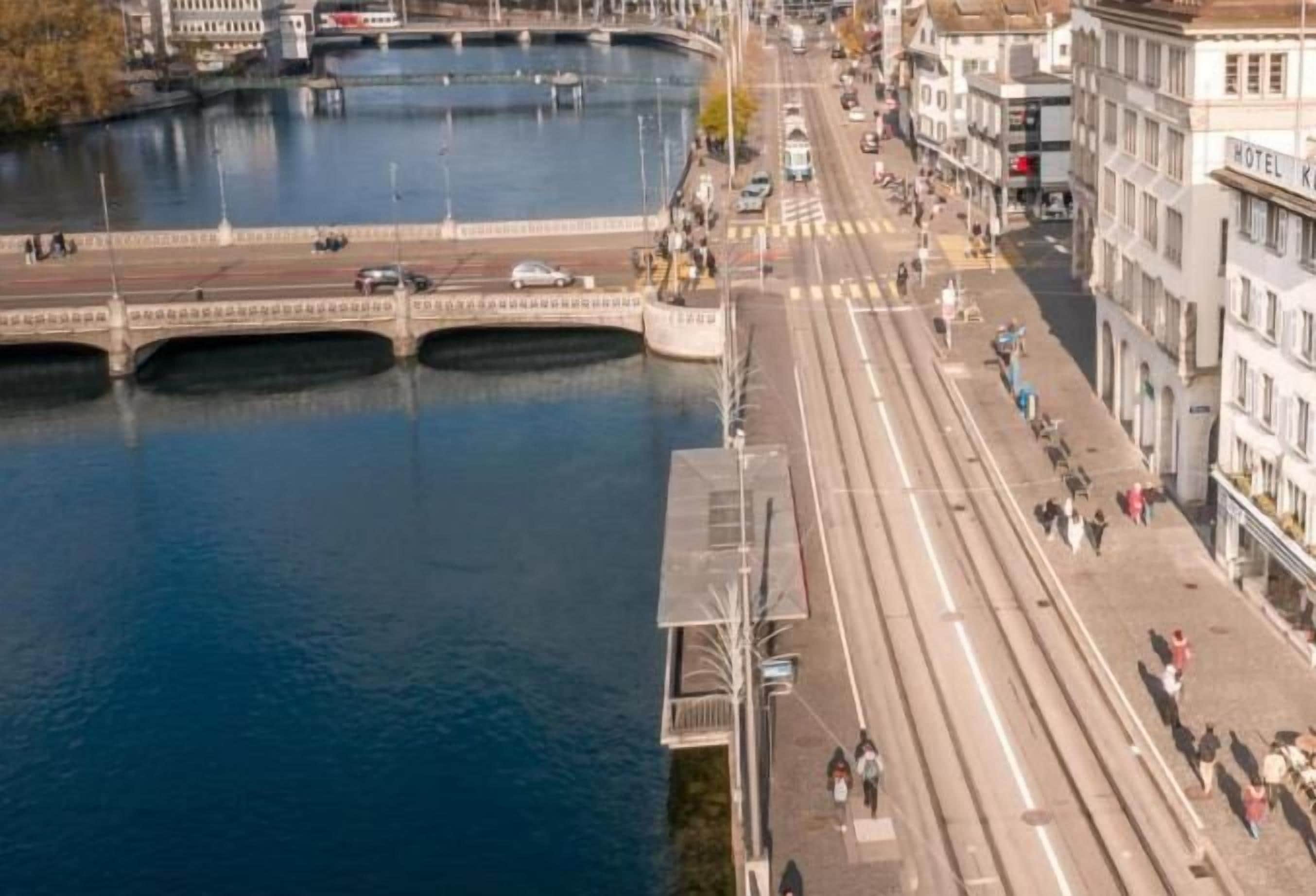 Une rivière traversée par un pont, bordée d’une promenade piétonne et de bâtiments.