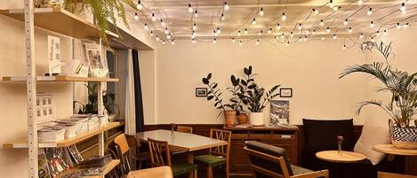 Um café acolhedor com móveis de madeira, lâmpadas pendentes e plantas em vasos.