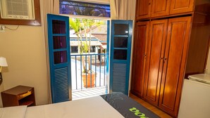A hotel room with a bed, a desk, a wardrobe, and a balcony with a view of a building and palm trees. - VOA Hotel Caxambu (Caxambu)