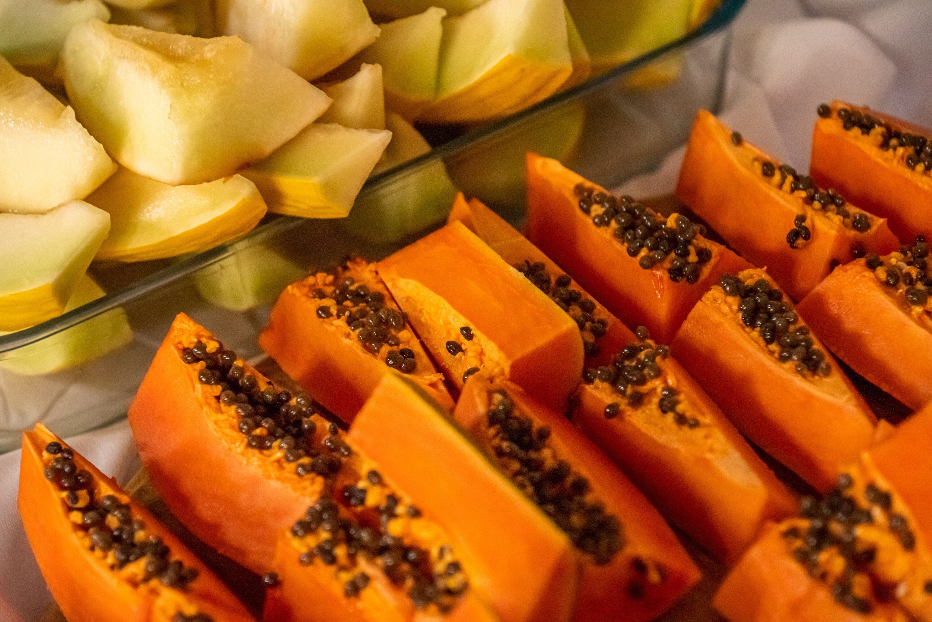 Un expositor de vidrio con papaya y melón en rodajas.