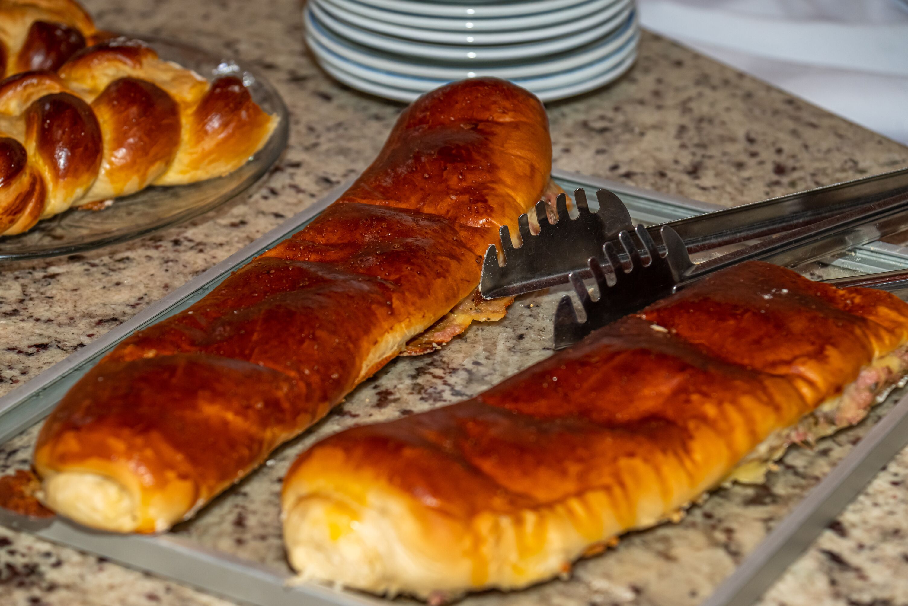 Uma salsicha assada e comprida sobre um prato de vidro.