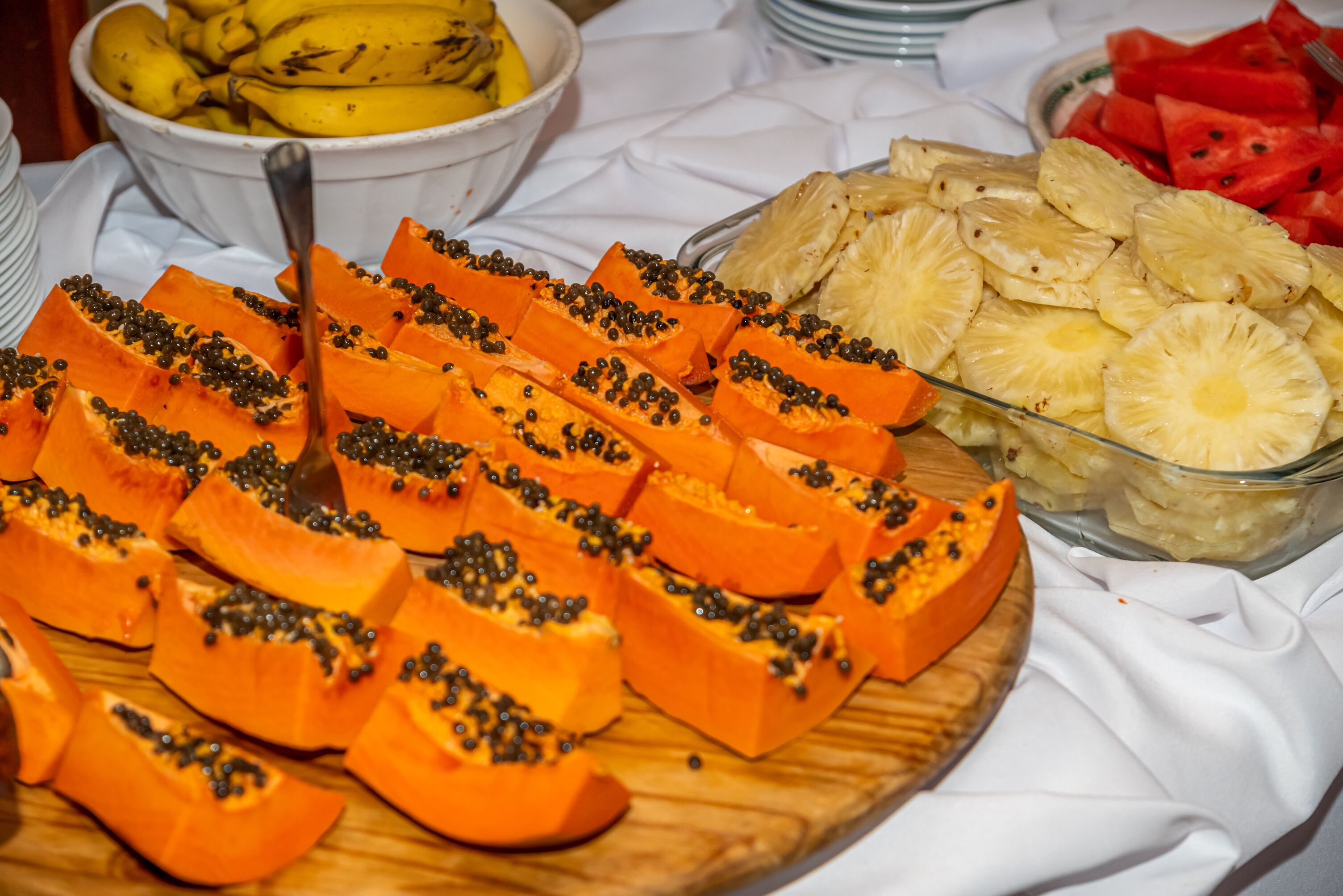 Et fad med frugter, herunder skiver af papaya og ananas, på en træplade.