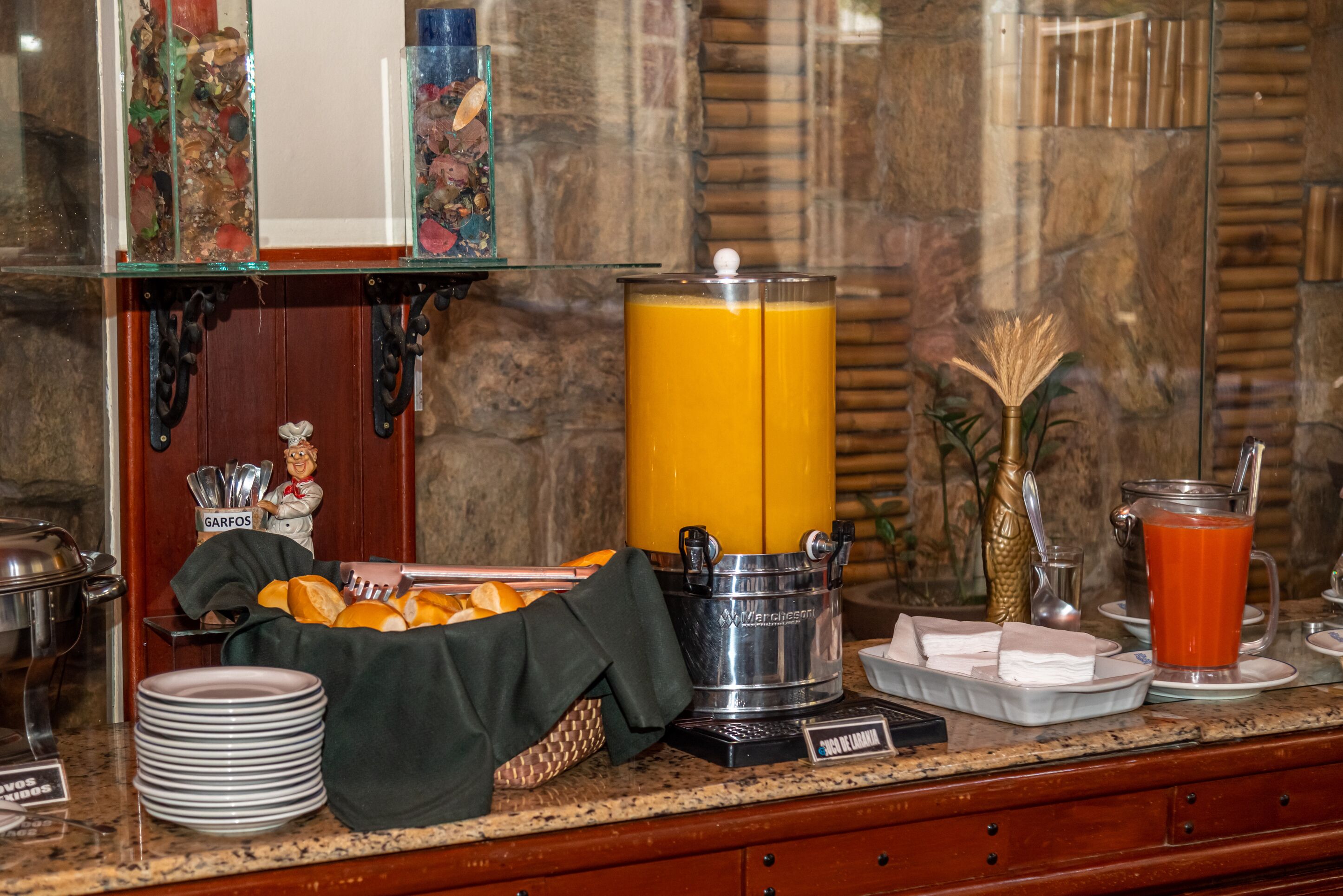 A breakfast buffet setup with a juice dispenser, bread, and a coffee machine.