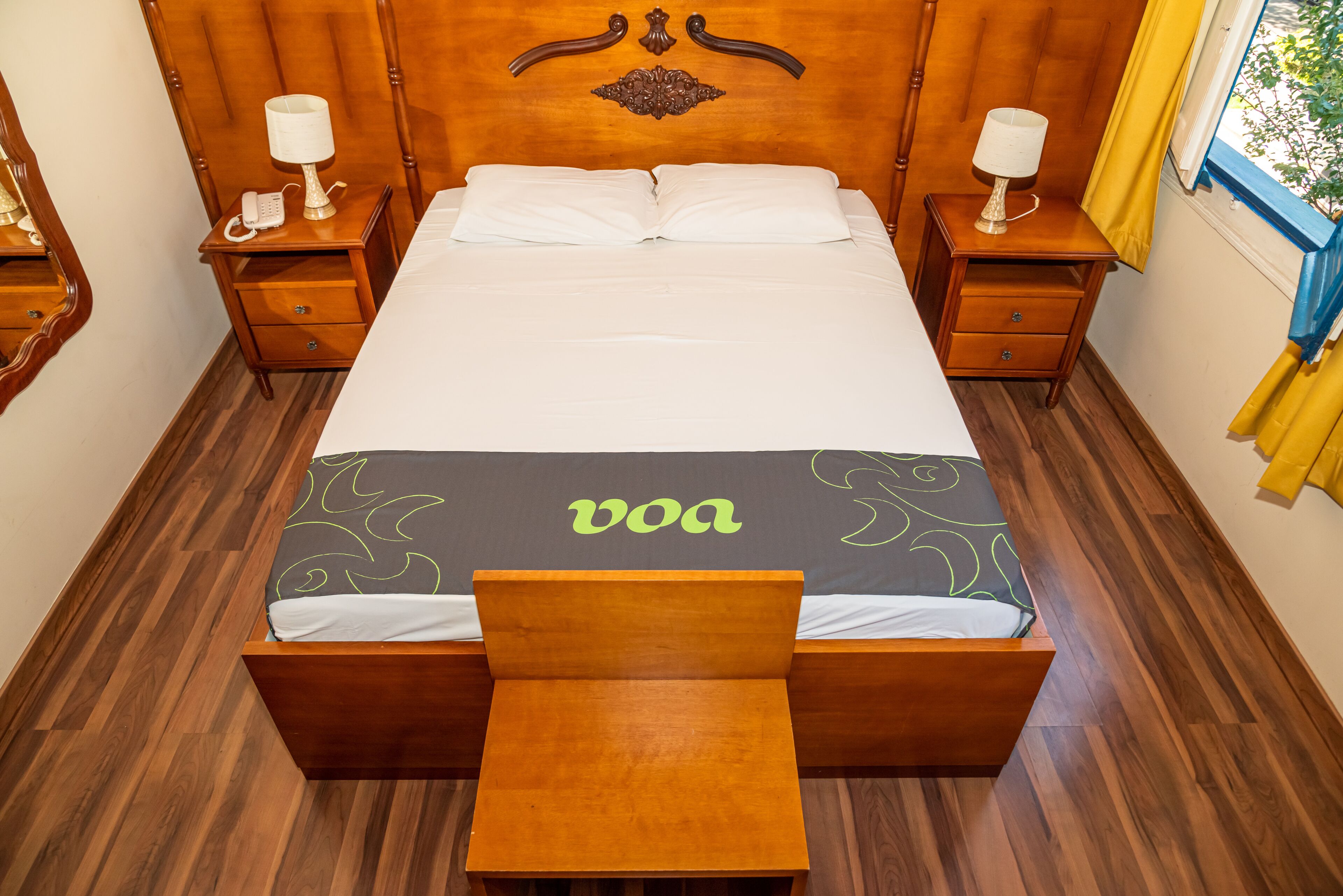 A neatly made bed with a headboard, two bedside tables with lamps, and a bench at the foot of the bed.