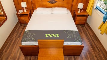 Una cama bien hecha con cabecera, dos mesitas de noche con lámparas y un banco al pie de la cama.
