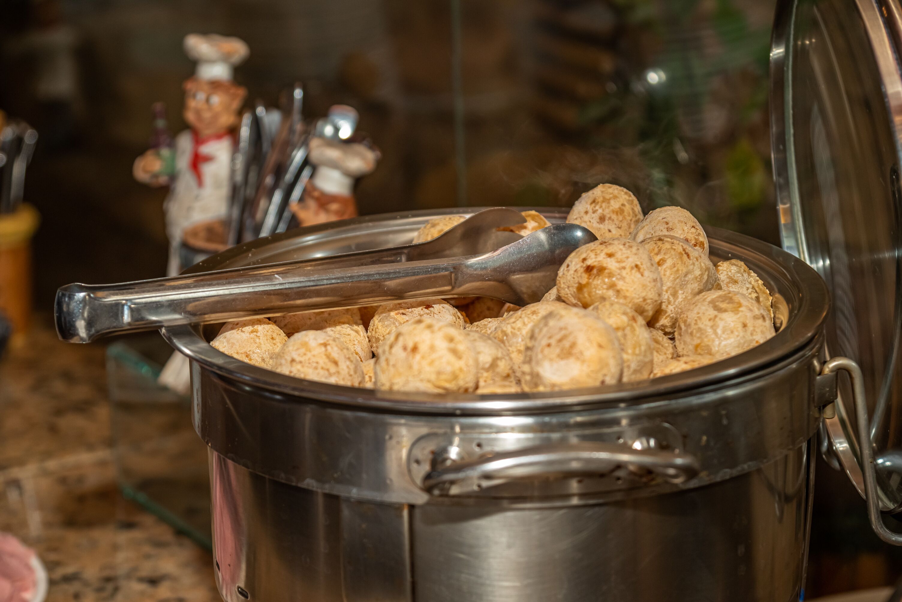 A stainless steel pot filled with round, golden-brown pastries, with a spoon resting on top.