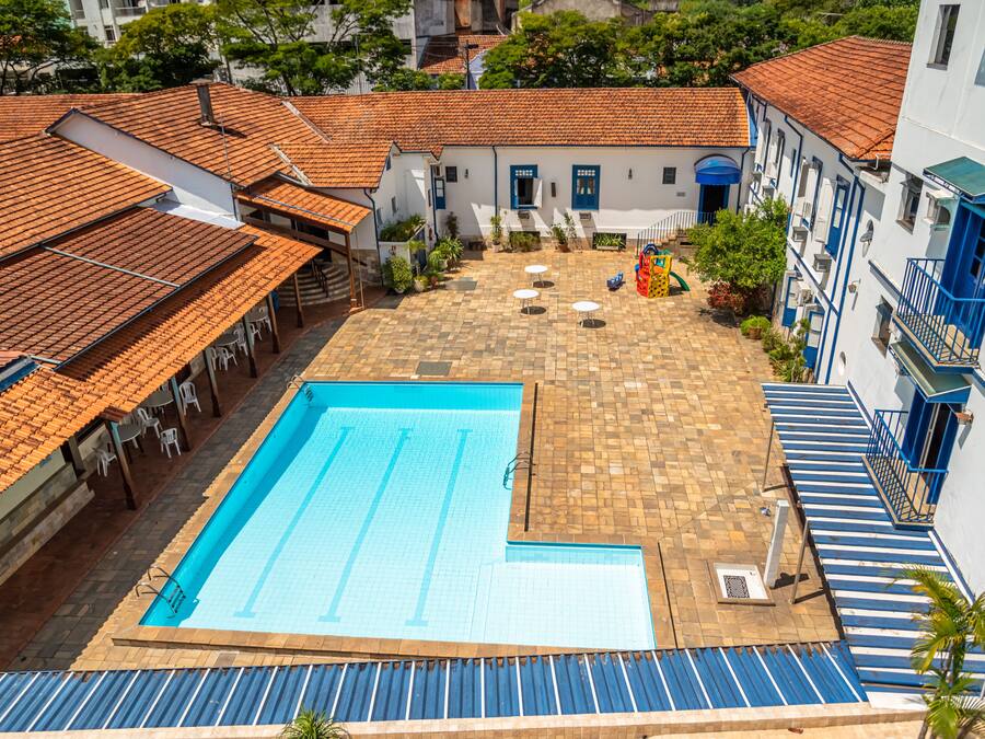 A swimming pool with a tiled deck, surrounded by buildings with red-tiled roofs and blue accents.