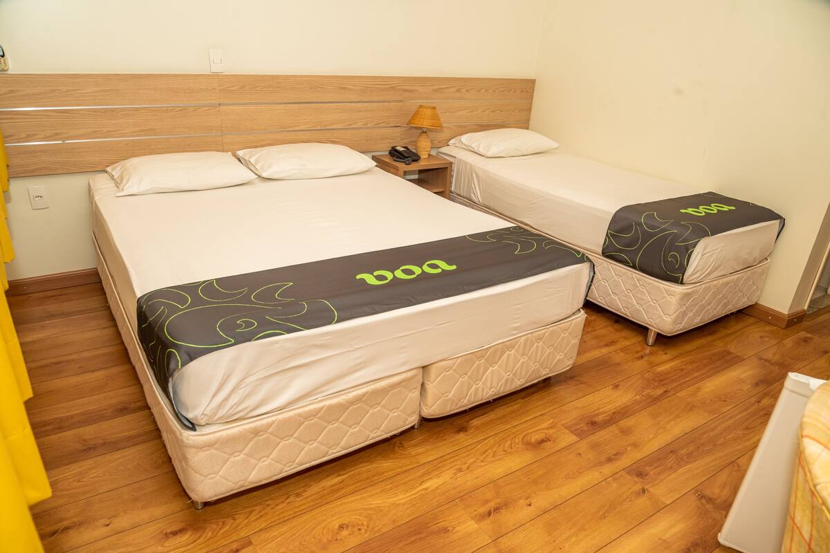 A hotel room with two beds, a wooden headboard, a nightstand with a lamp, and a yellow curtain.