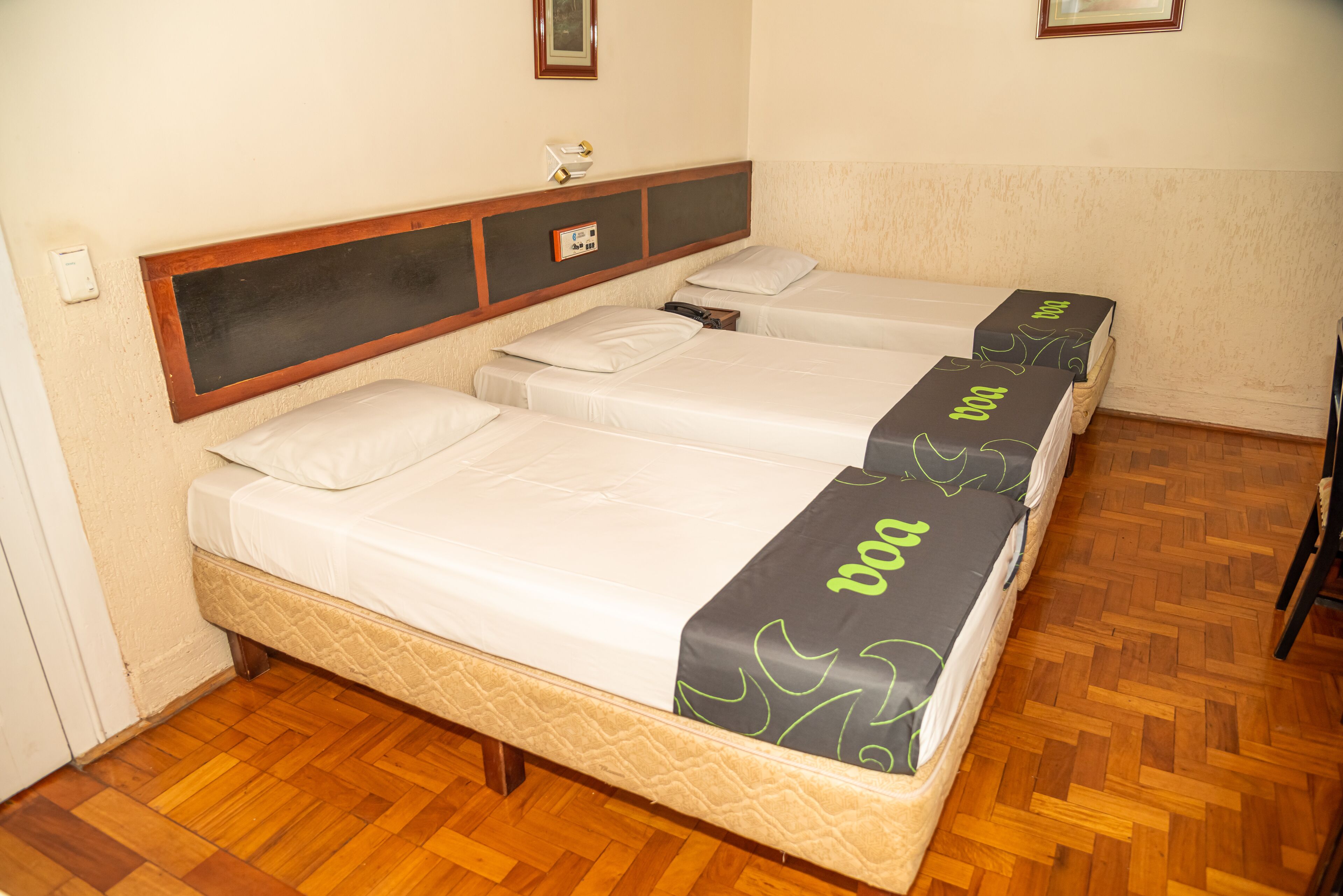 Habitación de hotel con tres camas individuales, cada una con una colcha gris y verde.