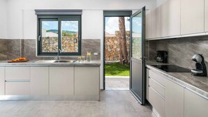 A modern kitchen with a large island, a stone wall, and a view of a garden.