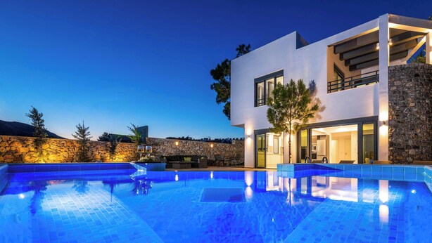 A modern two-story house with a swimming pool, stone wall, and outdoor seating area.