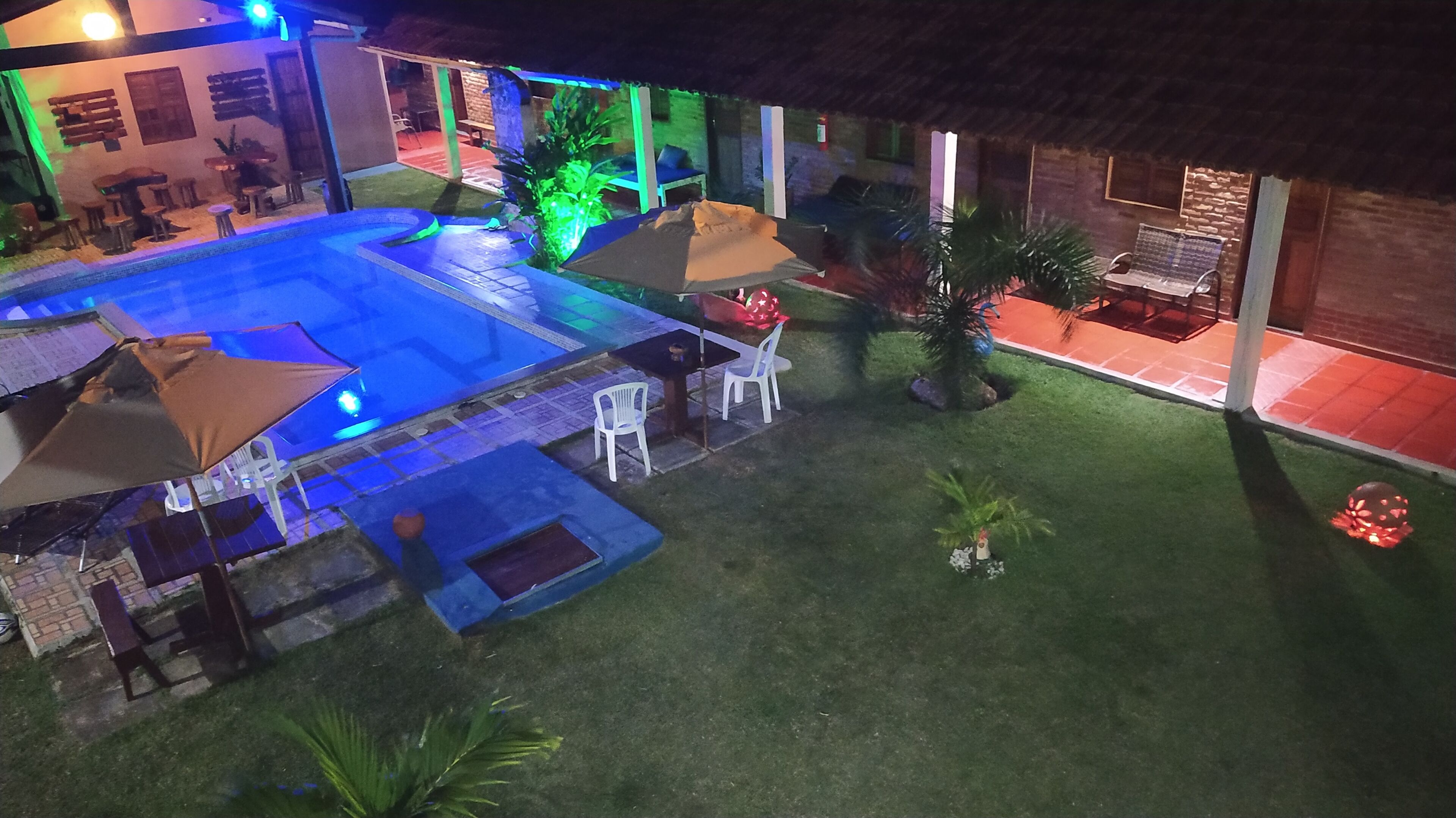 Un área de piscina con sillones de descanso y sombrillas, rodeada por un césped cuidado y un edificio de ladrillo.