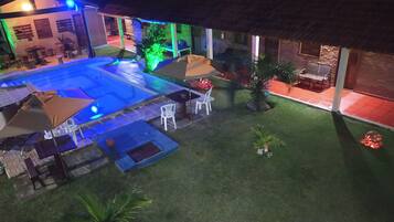 Un área de piscina con sillones de descanso y sombrillas, rodeada por un césped cuidado y un edificio de ladrillo.