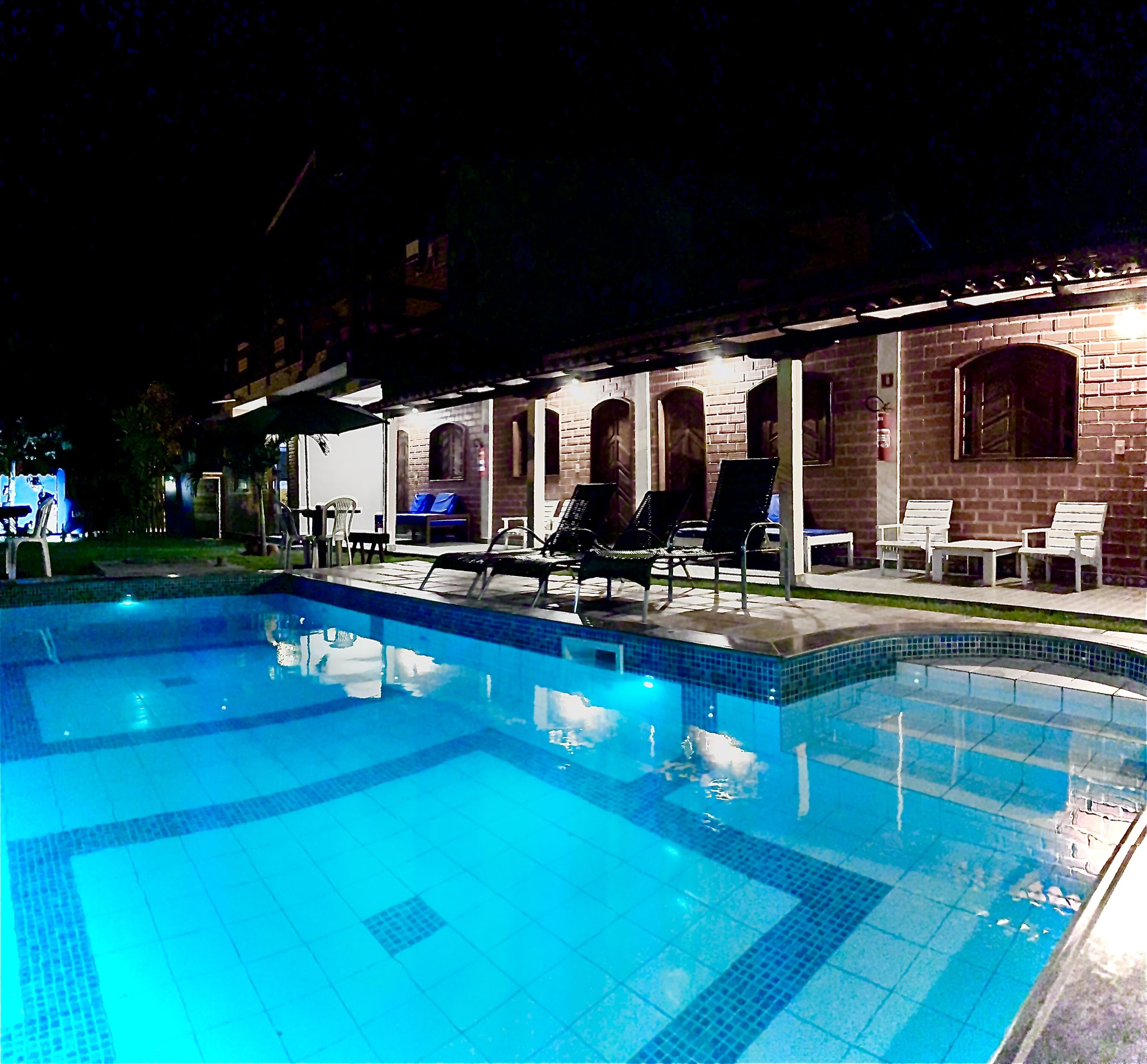 Una piscina con sillones de playa y un área de estar techada durante la noche.