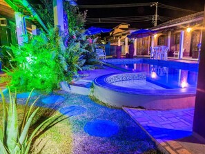 A swimming pool area with a hot tub, surrounded by a garden with various plants and a patio with chairs. - Pousada Askalon (Itaunas)